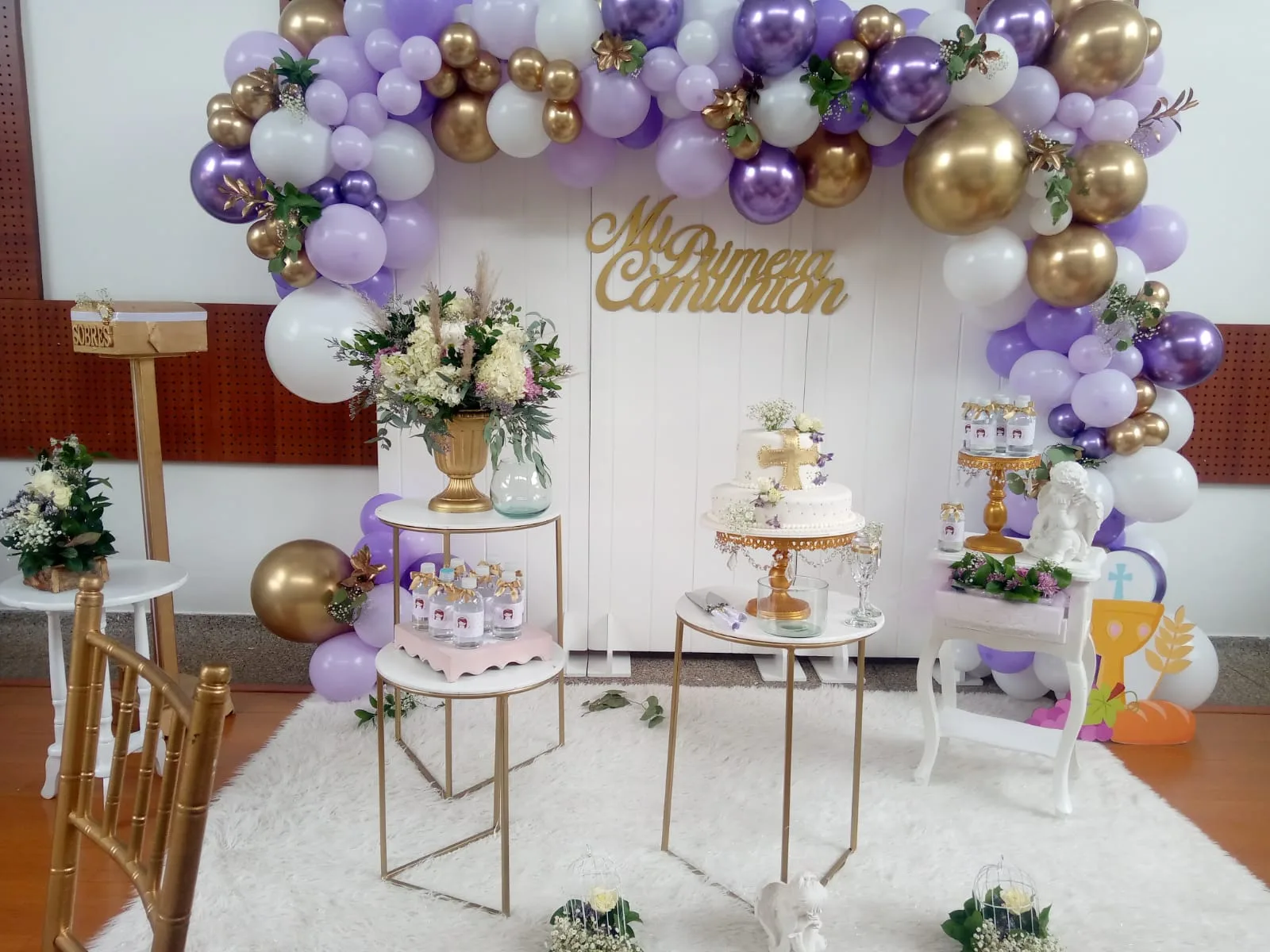 Montaje de primera comunión con arco de globos lila y dorado y mesa de ponqué